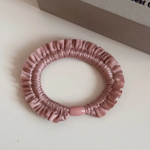 Detailed view of dusty pink silk elastic scrunchie with ruffled edges and resin buckle