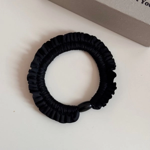 Close-up of black ruffled elastic hair tie with a decorative bead on cream surface