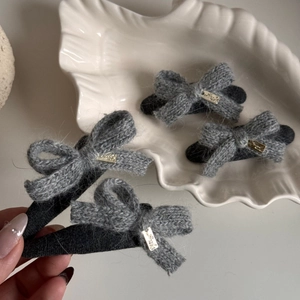 Grey knitted bow hair clip with metal lucky charm on a minimalist ceramic plate