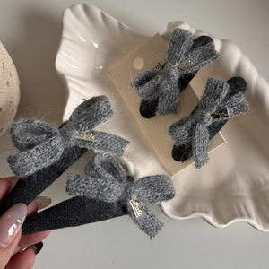 Grey knitted bow hair clips with gold metal accents on elegant white shell tray