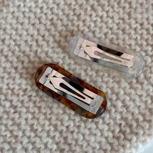 Detail view of two tortoiseshell and iridescent rectangle hair clips on beige knit fabric