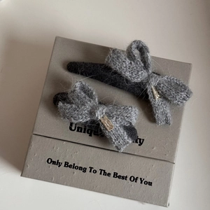 Close-up of gray knitted bow hair clips with gold metal accents in a gift box