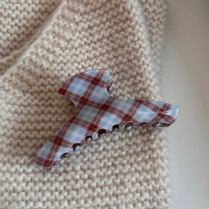 Detailed close-up of a large red plaid acetate hair claw clip on a soft knit fabric