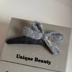 Macro shot of grey knitted bow hair clip with soft yarn texture and golden charm detail