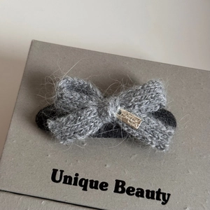 Macro detail of a grey knitted bow hair clip featuring soft texture and a metal accent