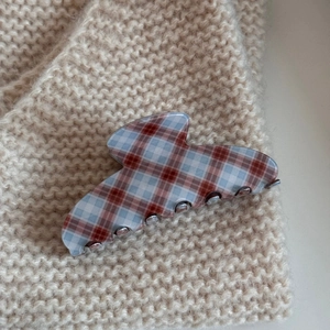 Macro detail of red and blue checkered acetate hair claw on beige knit background