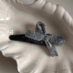 Close-up detail of knitted bow hair clip with metal charm on soft grey wool texture