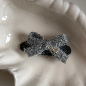 Macro shot of grey knitted bow hair clip with golden metal plate on a shell plate