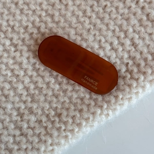 Close-up of brown amber acetate hair clip with golden handmade logo on knit fabric