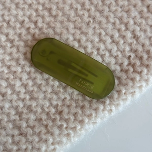 Detail of an oval olive green acetate hair clip on beige knit fabric background