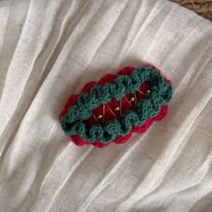 Détail d'une pince à cheveux tricotée rouge et verte avec perles dorées sur lin