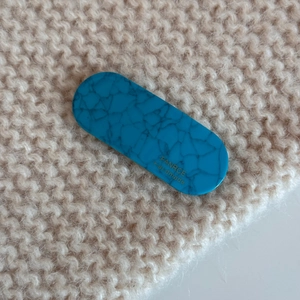 Macro detail of oval turquoise marble acetate clip on a soft beige knit background