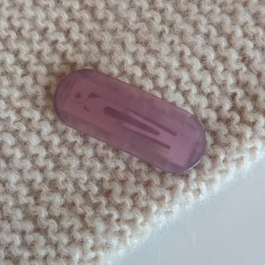 Macro shot of purple oval acetate hair clip with gold logo on beige knit texture