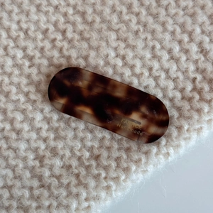 Detail of oval acetate hair clip with tortoiseshell texture on beige knit background
