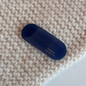 Detail of a dark blue acetate hair clip with gold handmade lettering on knit background