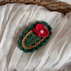 Détail d'une pince à cheveux tricotée verte avec une fleur rouge et une perle