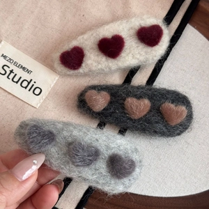 Detailed close-up of three plush heart-shaped hair clips in white, dark grey and light grey