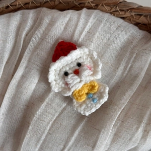 Détail d'une pince à cheveux bonhomme de neige au crochet avec bonnet rouge tricoté