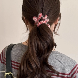 Détail de l'élastique à cheveux en peluche rouge et blanc sur cheveux bruns ondulés