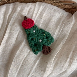 Détail d'une pince à cheveux sapin de Noël tricotée main avec perles sur tissu beige
