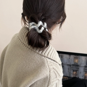Détail d'un chouchou en peluche tricotée blanche porté sur un chignon brun élégant