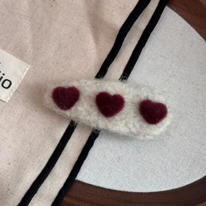 Macro shot of plush cream-colored hair clip featuring three soft burgundy heart details