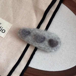 Detail of plush grey heart hair clip showing soft wool texture on a beige canvas surface
