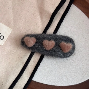 Detail of plush grey hair clip featuring three brown 3D hearts on a textured canvas bag