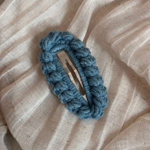 Close-up of hand-knitted blue crochet hair clip with textured wool on soft beige linen
