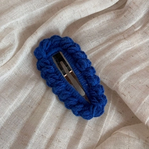 Detail of royal blue hand-knitted crochet hair clip with textured wool yarn on fabric