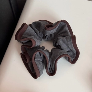 Macro view of grey knit scrunchie with brown contrast piping and pleated texture