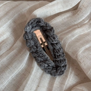 Detailed view of handmade dark grey wool knit hair clip on a beige linen fabric texture