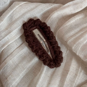 Detailed view of dark brown hand-knitted crochet hair clip with wavy textured edges