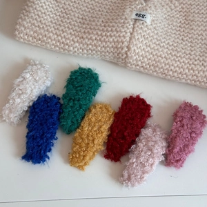 Set of seven plush lamb wool hair clips in vibrant colors on a cozy knit background