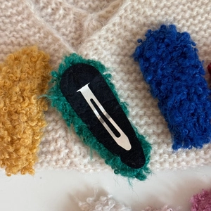 Detail showing the green plush hair clip with silver metal snap and black felt backing