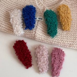 Colorful lamb wool hair clips in seven vibrant colors on soft beige knit background