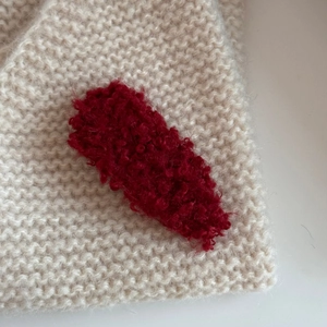 Close-up of a handmade red fuzzy knitted BB hair clip on soft beige knit fabric