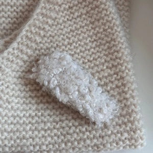 Macro shot of white plush lamb wool hair clip showcasing soft texture on knitted fabric