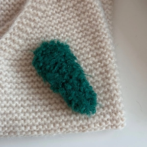 Detail of dark green plush hair clip with fuzzy texture on a beige knit background
