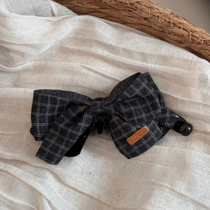 Detail view of handmade grey plaid fabric bow hair clip with leather label on linen
