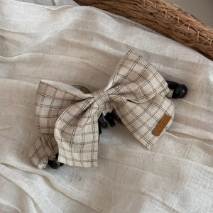 Close-up of beige plaid fabric bow banana clip with a handmade leather label