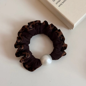 Leopard print scrunchie with large white pearl detail on a minimalist surface