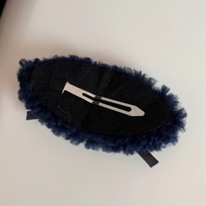 Detail view of the back of a dark blue plush hair clip with a sturdy metal fastener