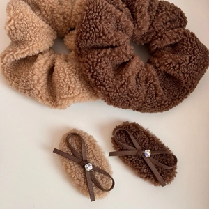 Detailed view of oversized plush scrunchies and bow hair clips in brown and beige fleece