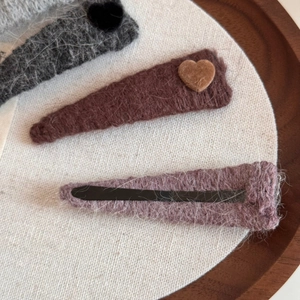 Detail of wool knit heart hair clips in grey and brown on a minimalist wooden tray