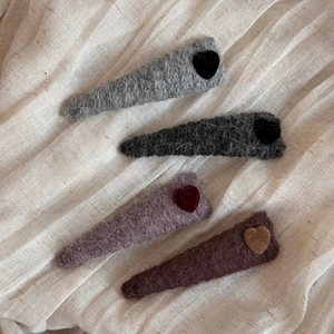 Close-up of four wool knit triangle hair clips with flocked heart details on linen fabric