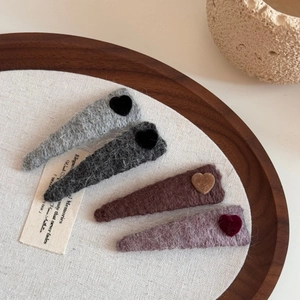 Set of four knit triangle hair clips with contrast heart patches on a wooden tray