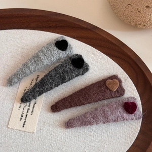 Set of four fuzzy knit triangular hair clips with heart accents on a rustic tray