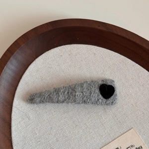 Close-up of grey knitted triangle hair clip with a black velvet heart on wood base