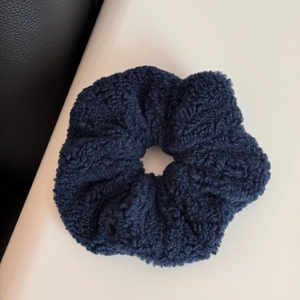 Detail of navy blue knitted plush scrunchie with thick textured elastic fabric